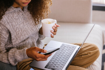 Young woman with cup of coffee using gadgets at home