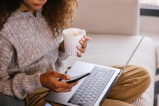 Young woman with cup of coffee using gadgets at home