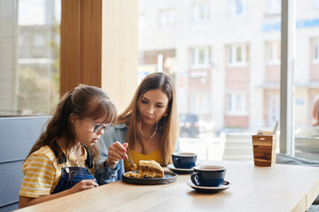 Warm-toned portrait of caring mother and daughter with down syndrome enjoying cakes in cafe, copy space