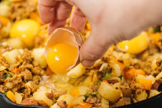 Pouring a cracked egg over a Mexican breakfast hash dish