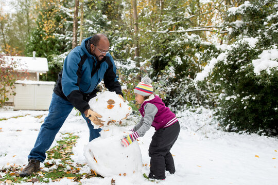 Father lifts snowball onto snowman with daughter - Powered by Adobe