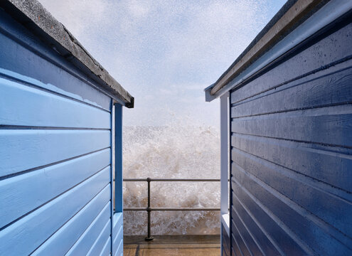 Waves and spray between beach huts. Southwold, Suffolk, UK.