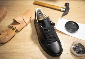 a black branded boot, a wooden block, a hammer, lie on the work table of a shoemaker in the workshop. Armani brand shoes