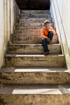 Handosme boy sits on sunny concrete steps