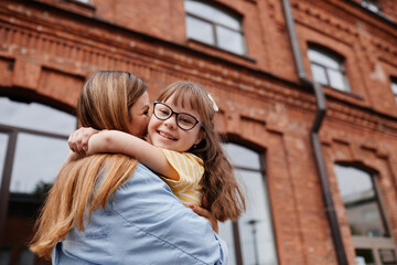 Candid portrait of happy girl with down syndrome embracing mother outdoors in city, copy space