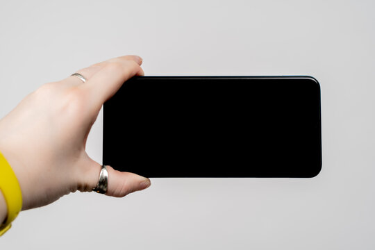 Cropped Woman Hand Holding Smartphone With Blank Screen Horizontally On White Background