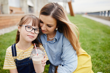 Portrait of loving mother and daughter with down syndrome embracing outdoors together, copy space