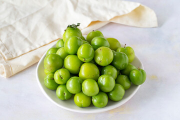 Ripe fresh green plums on a white ceramic plate