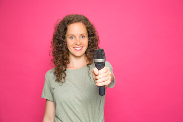 young woman with microphone in hand and green t-shirt on pink background