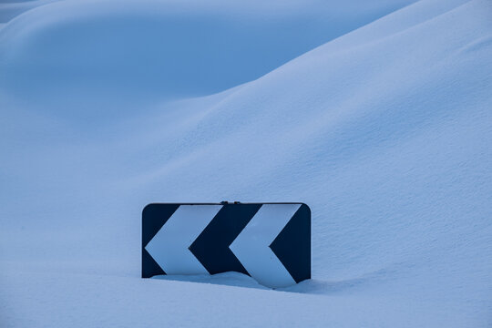 road sign of sharp turn buried in snow