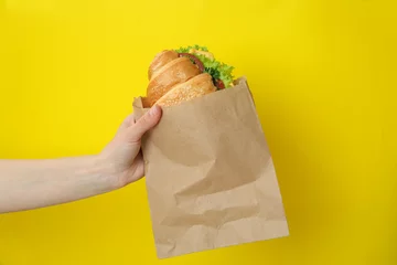 Fotobehang Vrouwelijke hand houdt croissantsandwich op gele achtergrond © Atlas
