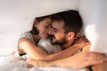 Young couple cuddling under the bed sheets.