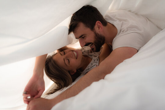Young couple cuddling and smiling under the bed sheets