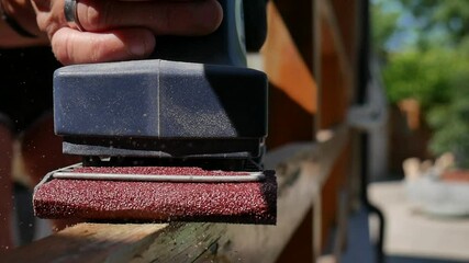 hand of carpenter using electric wood sander with sandpaper sanding a wooden