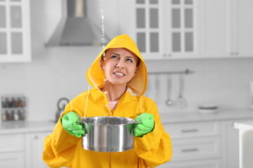 Young woman in raincoat collecting leaking water from ceiling at home. Time to call roof repair...