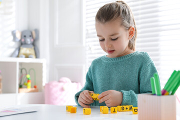 Little girl assembling word with yellow bricks in classroom at English lesson