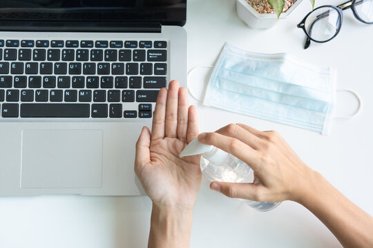 Top view of Asian woman hands apply sanitizer gel to disinfect hands with medical face mask over a work desk in office. Preventive measures during the period of pandemic and social exclusion.