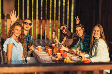 group of young friends are sitting at the table, drinking beer drinks and having fun in nature, friends doing barbecue in the backyard during dinner