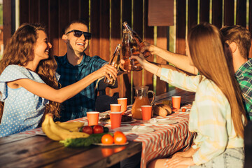 Group of young friends having lunch outdoors, friends celebrate and make toast at the table outdoors at sunset on a summer day