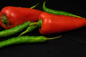 Red and green peppers on a black background. Black fabric background in folds. High quality photo
