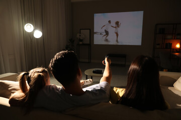 Family watching movie on sofa at night, back view