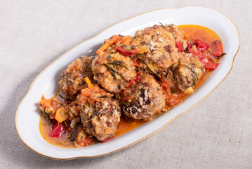 Meatballs in sauce baked with cheese in an oval plate on a table with a linen tablecloth, top view