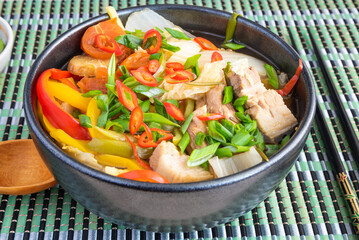 Thick soup with vegetables and pork with pepper and green onions in a black bowl on a bamboo napkin, close-up, Chinese cuisine.