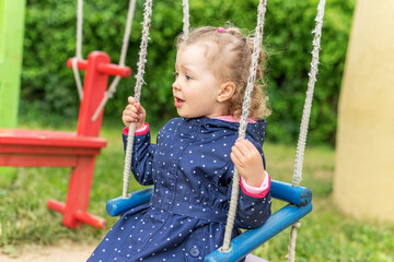 Little joyful girl swinging on a swing.