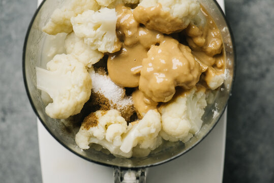 Food processor filled with cauliflower, cumin, salt, and tahini sauce