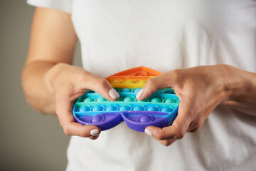 A close-up photo of a fidget toy "Pop it" in the shape of a heart in the hands of a girl. A young woman in a white t-shirt is pressing down bumps and relaxing.