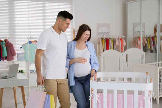 Happy pregnant woman and her husband with shopping bags choosing crib in store