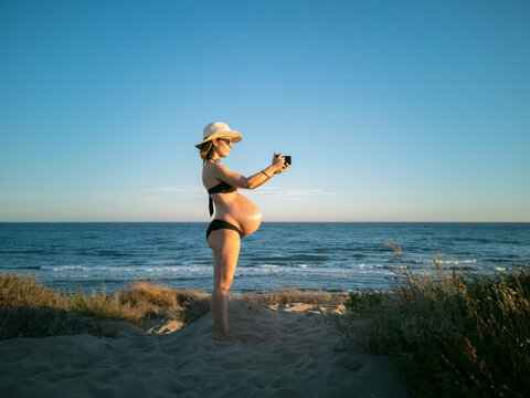 Pregnant woman taking photographs with her camera on the beach