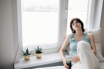 Woman with cup of drink relaxing on bed
