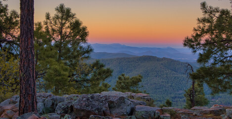 In Payson, Arizona this is known as the Mogollon Rim. The sun sets looking out over the rim, through the trees, the colorful sky paints the ledge and flowing hills, boulders and trees colorful shades 