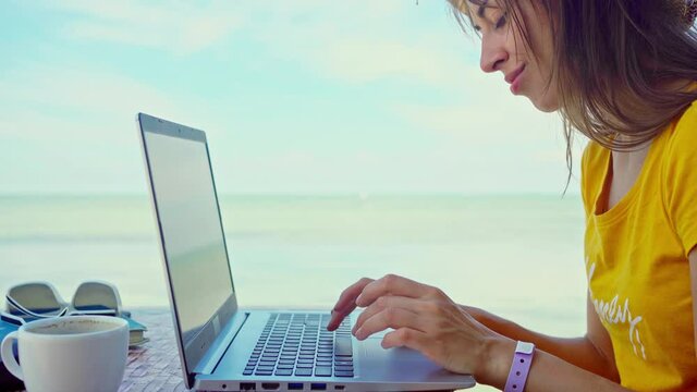 Concentrated woman working outdoors by blue sea on laptop computer