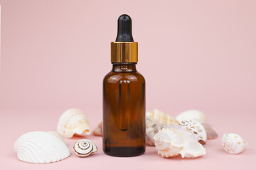 Fototapeta na wymiar Dropping essential oil into glass bottle or bottle of hyaluronic acid with pipette, many different sea shells on pink background. Serum for facial skin. Unbranded herbal mineral cosmetic. Front view.