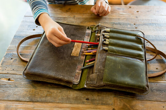 Boy pulls red pencil from leather porfolio