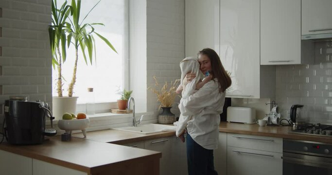 Mother and daughter spend time at home together. Young mom wipes her adorable little child after bathing in a kitchen sink. Woman holds adorable child wrapped in a towel.