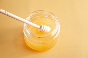 Honey jar with dipper on yellow background.