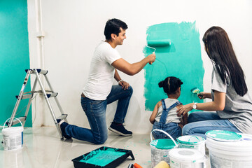 Happy asian family using a paint roller and painting walls in their new home