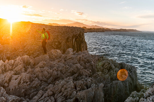 Male hiker taking selfie in rocky scenic seacliff at sunset 