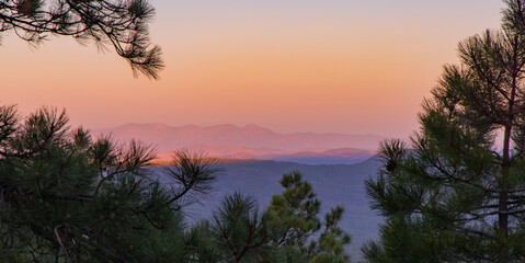 Fototapeta na wymiar In Payson, Arizona this is known as the Mogollon Rim. The sun sets looking out over the rim, through the trees, the colorful sky paints the ledge and flowing hills, boulders and trees colorful shades 