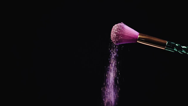 sparkling pink glitter falling down from soft cosmetic brush on black