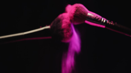blurred cosmetic brushes making explosion of pink powder on black background