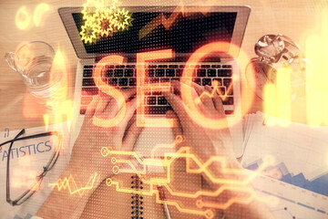 Multi exposure of man's hands typing over computer keyboard and SEO hologram drawing. Top view....