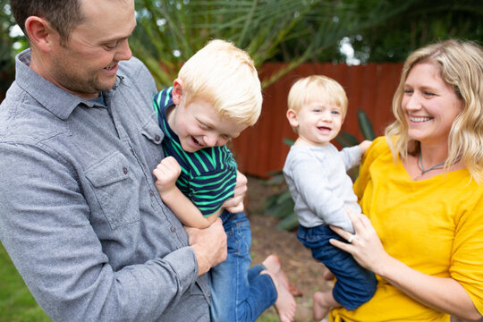 Laughing parents holding wriggling young sons in backyard
