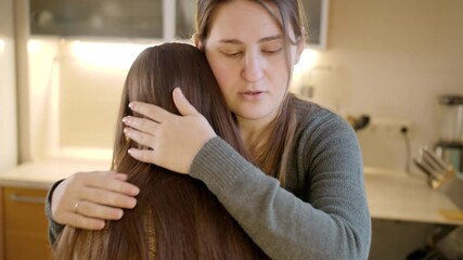 Young mother kissing and hugging upset crying daughter after talking about problems. Parent supporting and comforting child - Powered by Adobe