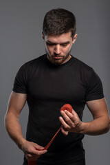 Relaxed sporty guy rolling up boxing tape after punching workout