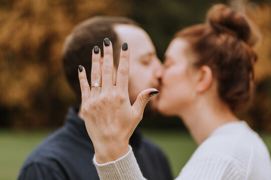 Fiance Showing off Engagement Ring and Couple Kissing in Background