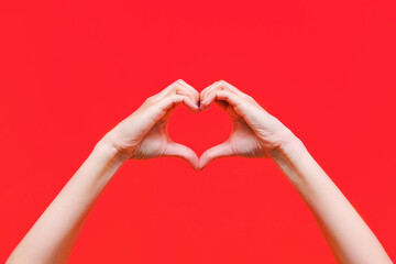 Female hands showing a heart shape isolated on a bright color red background. Sign of love,...
